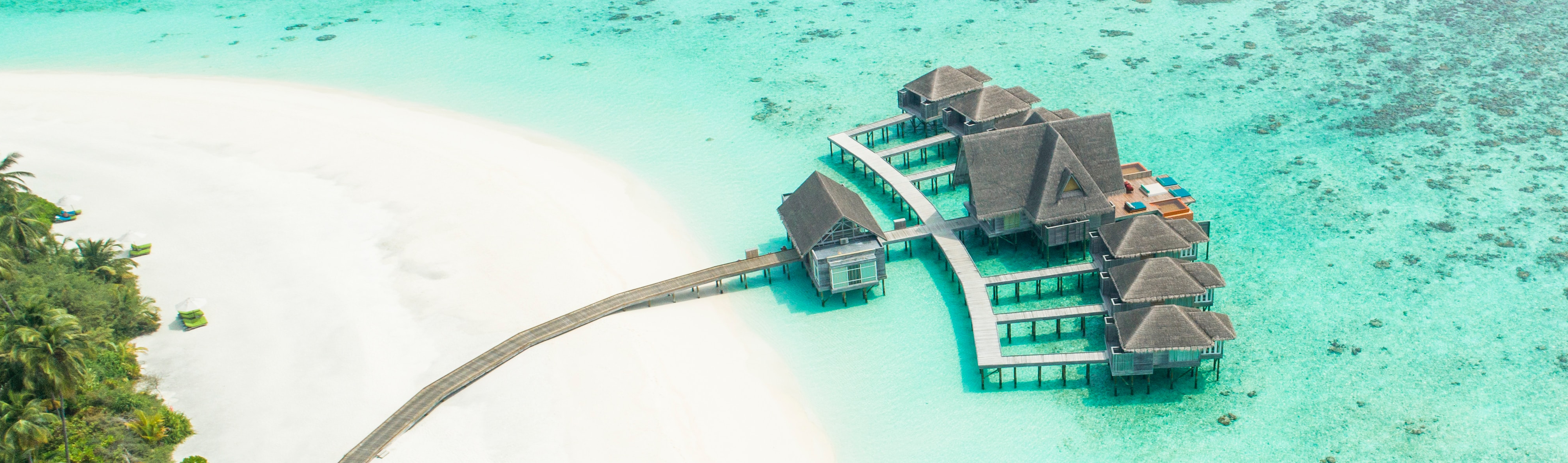 Aerial view of luxury overwater villas connected by wooden walkways on a white sand beach and turquoise lagoon in the Maldives.