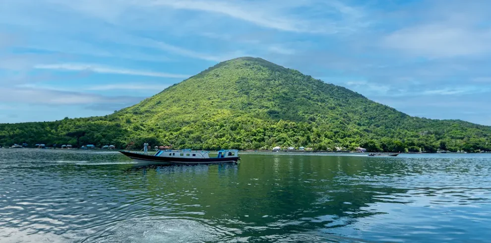 Scenic view of a stunning hill rising above the crystal-clear waters of Banda Sea during our liveaboard expeditions