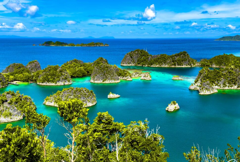 A stunning aerial view of Piaynemo in Raja Ampat, showcasing vibrant turquoise waters, lush green karst islands, and a clear blue sky