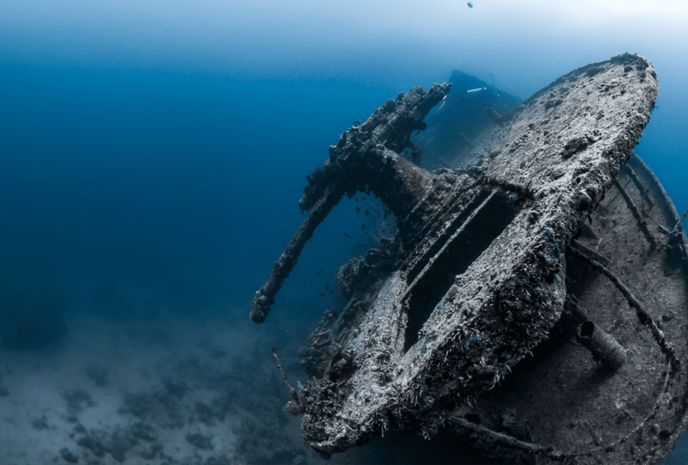 A hauntingly beautiful shipwreck submerged in the depths of the Red Sea, covered in marine life and resting on the sandy seafloor.