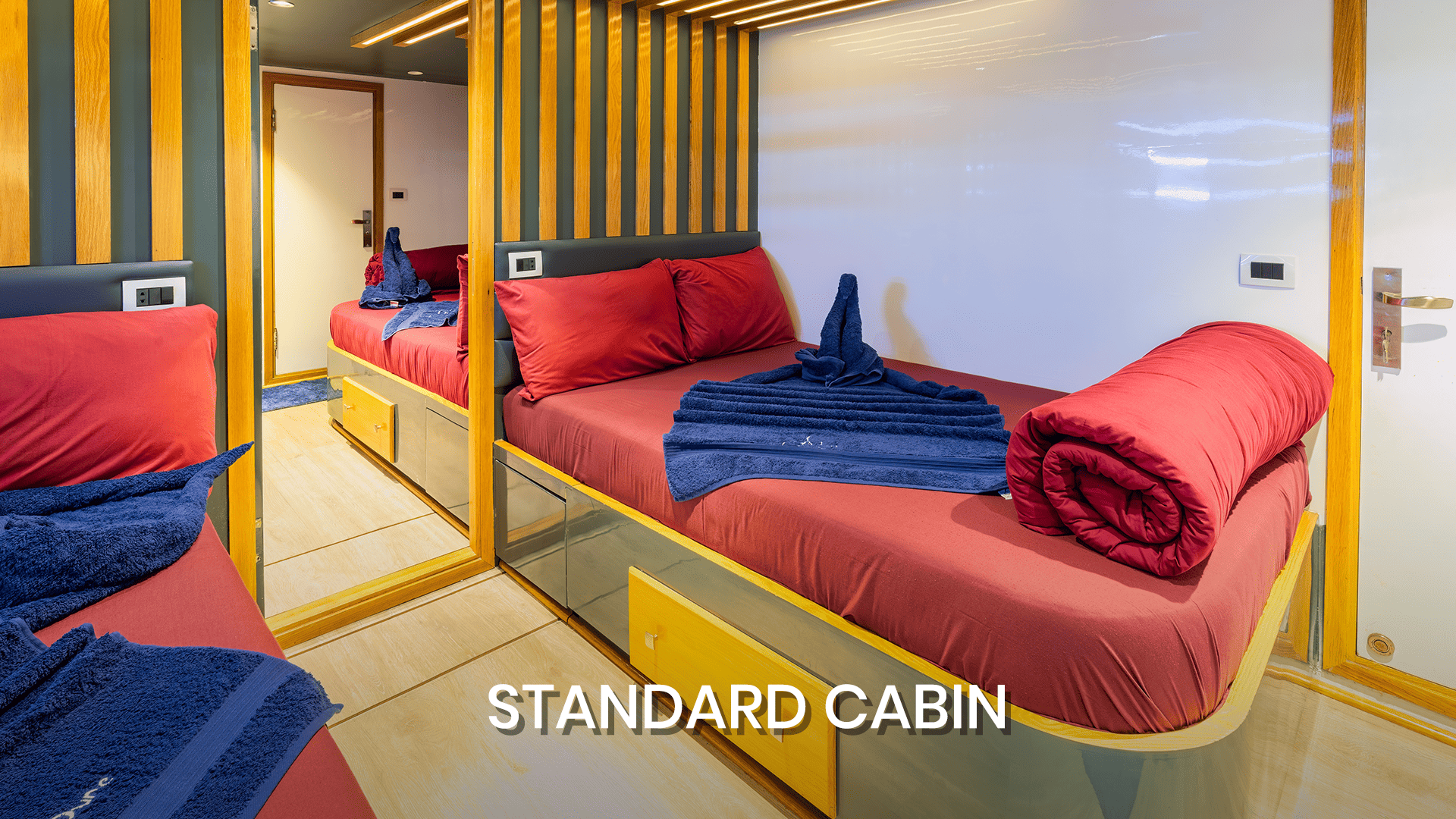 Standard cabin Dune Silky liveaboard featuring twin beds, modern mirror design, and comfortable red bedding