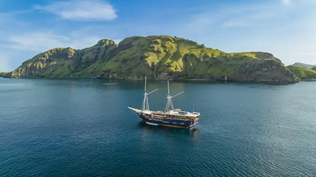 Aurora liveaboard sailing near lush green cliffs in the Banda Sea, Indonesia.