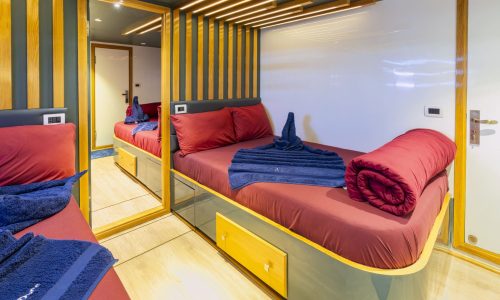 Standard cabin Dune Silky liveaboard featuring twin beds, modern mirror design, and comfortable red bedding